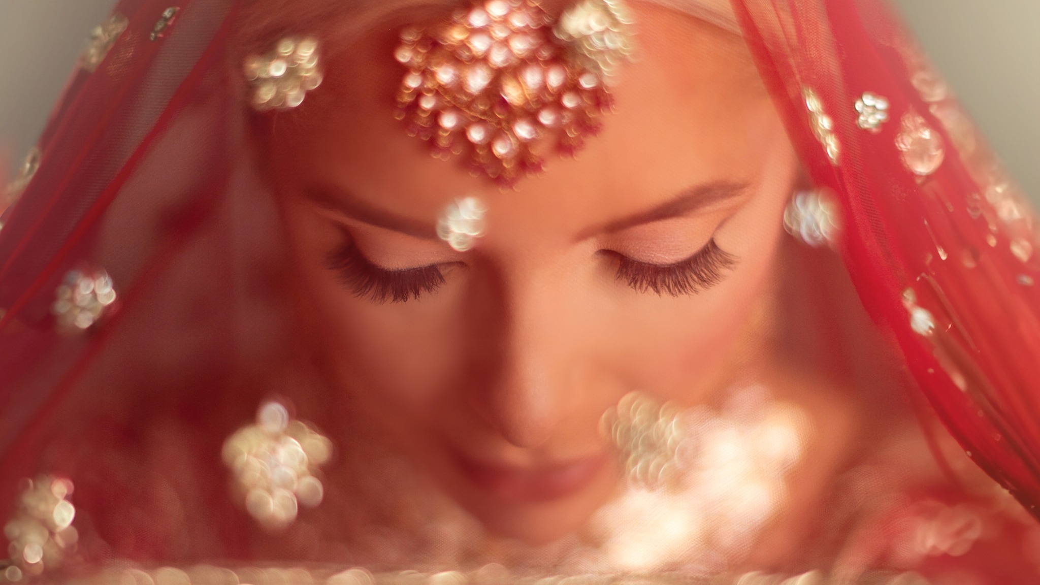 Close portrait of a South Asian bride beneath a red dupatta with traditional jewellery
