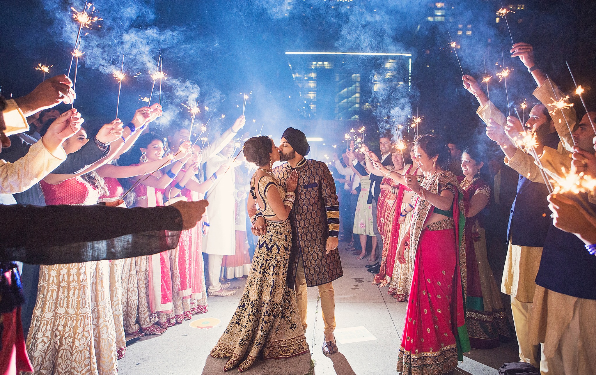 Newlywed South Asian couple kissing beneath sparklers during a nighttime wedding exit