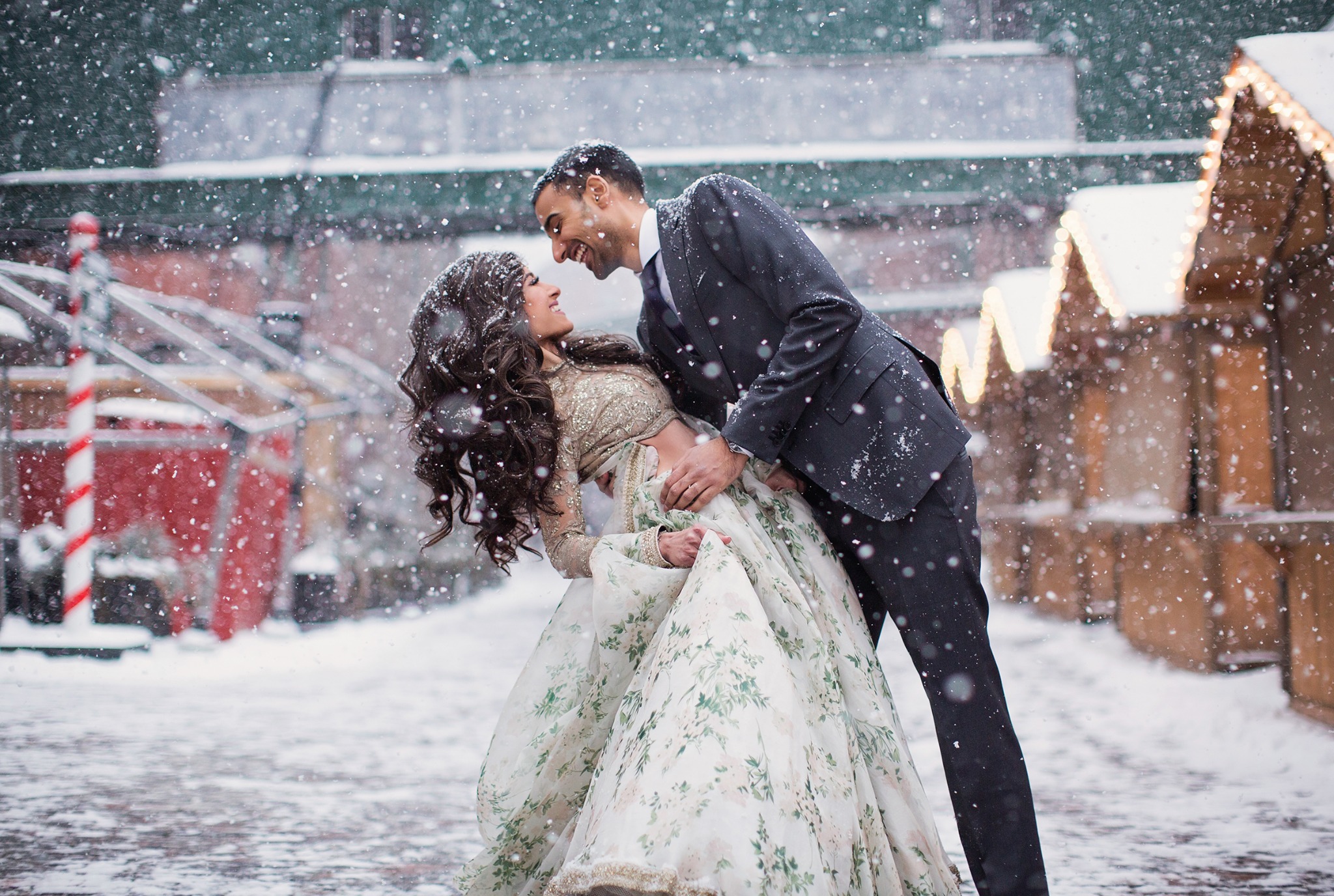 Couple sharing a joyful portrait in falling snow during a winter wedding celebration