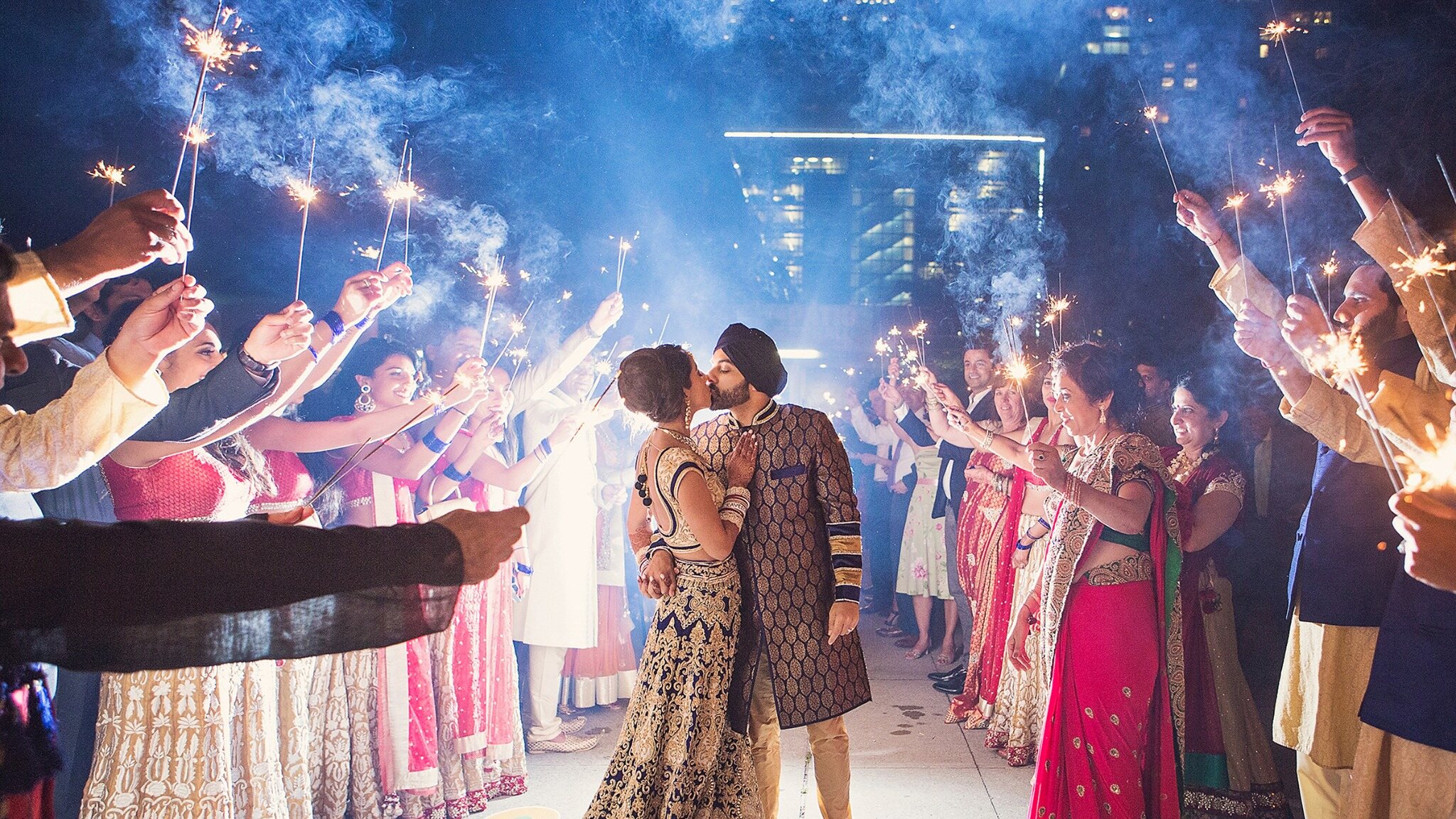 South Asian newlywed couple celebrating beneath sparklers during a nighttime wedding exit